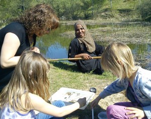 Två pedagoger och två barn sitter vid sjökanten.