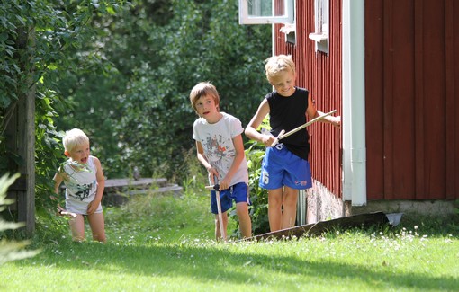 Barn smyger vid husknut med träsvärd i händerna.