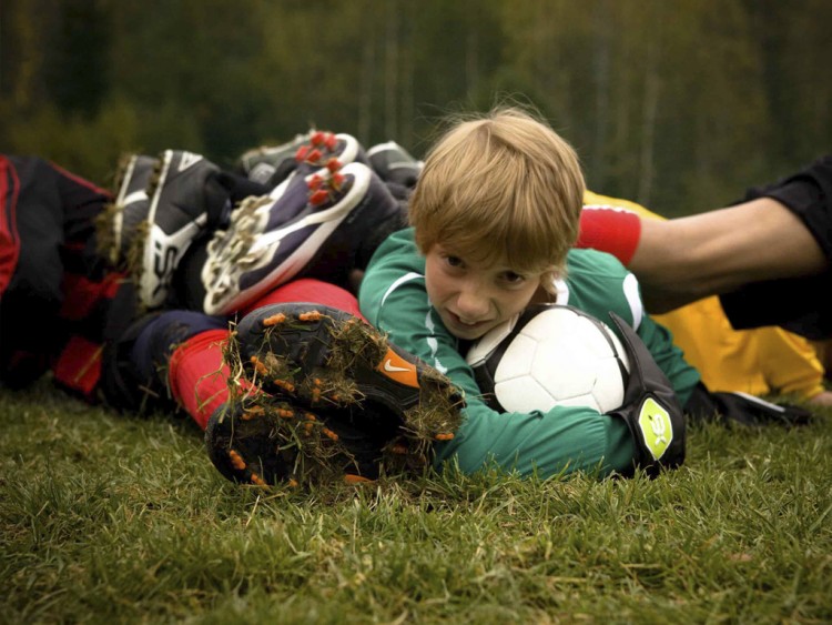 Pojke som ligger unders i hög av fotbollsspelare håller i fotboll.