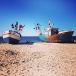 Två rostiga båtar ligger på en sandstrand.