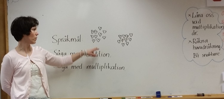 Pedagog står vid tavla och pekar på text.