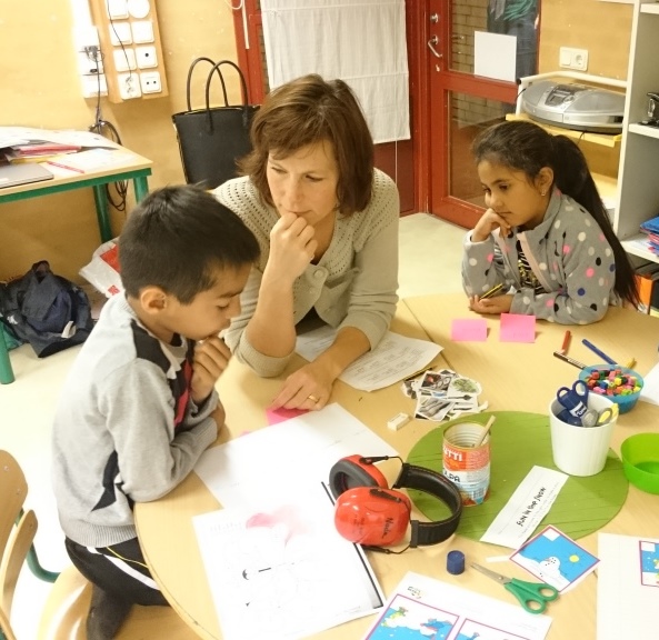 Pedagog sitter med två barn vid bord.