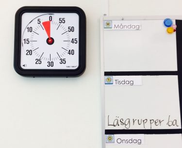 En timer bredvid whiteboard där dagens schema står.