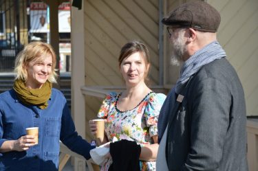 Två kvinnor och en man dricker kaffe och samtalar utomhus.