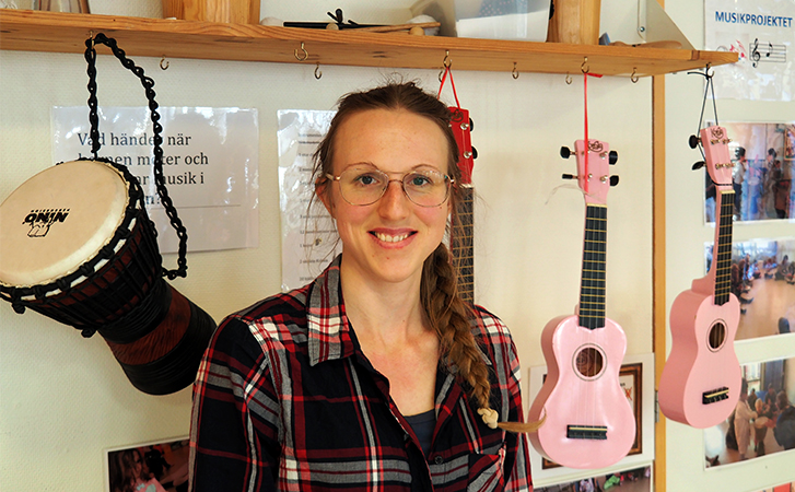 Kvinna sitter framför upphängda trummor och ukuleles.