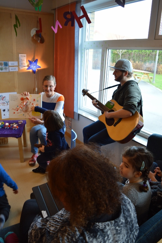 Man med gitarr och kvinna med uppslagen sitter framför barn i publiken.