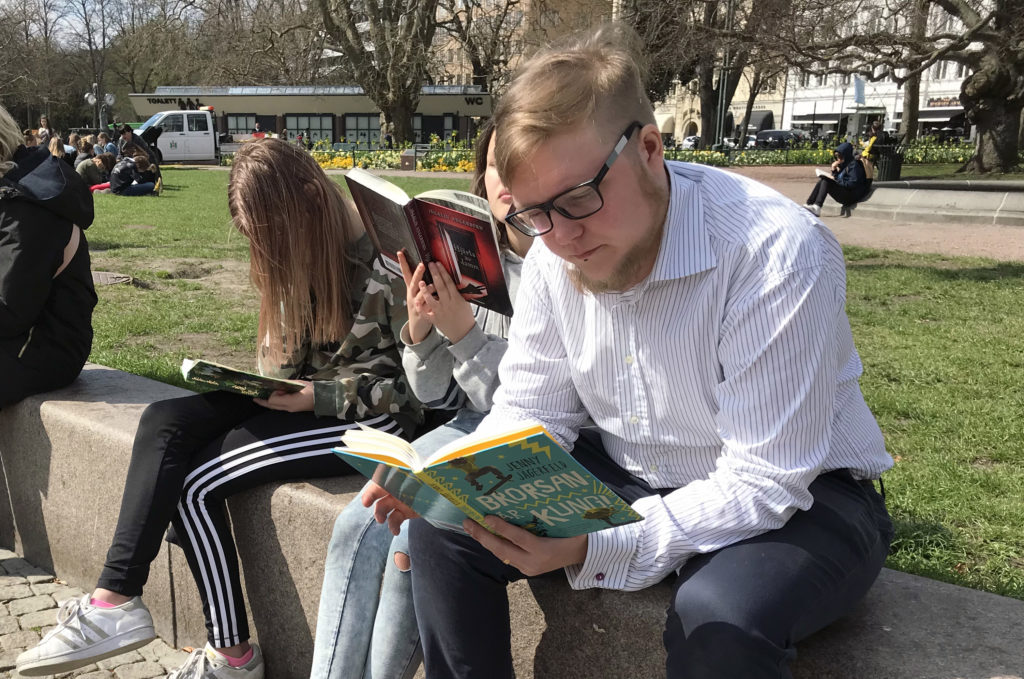 Skolbibliotekarie och elever sitter och läser på stenbänk i Malmö.