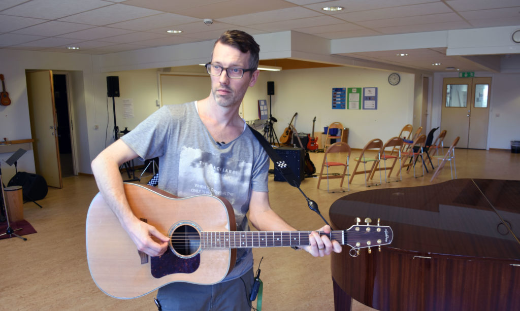 Man med gitarr i musiksal.