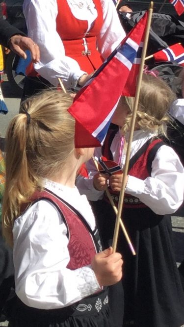 Två små barn i norska folkdräkter viftar med norsk flagga.