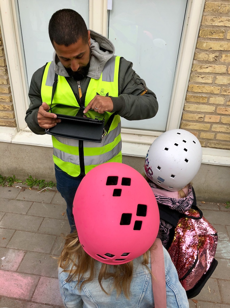 Rastvakt med reflexväst checkar in barn som står i kö framför honom på sin läsplatta.