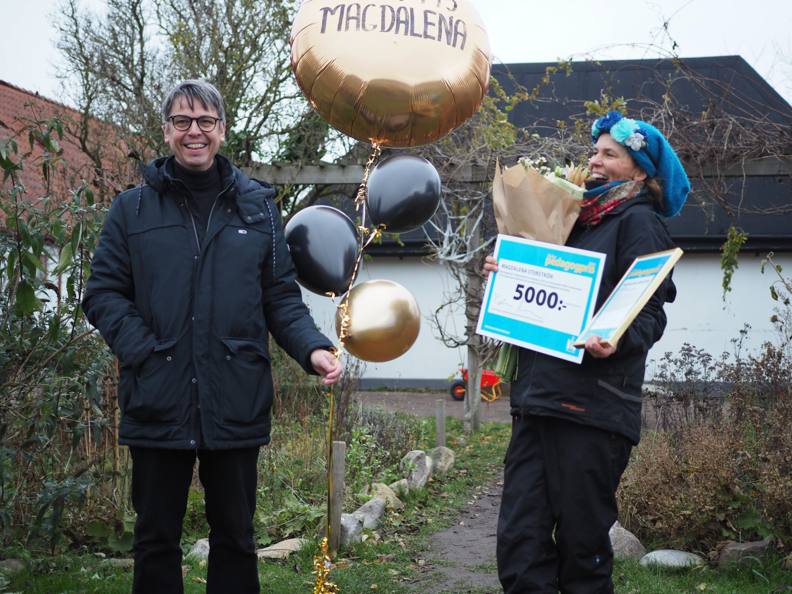 Direktör håller ballonger och överraskad pristagare håller check och diplom.