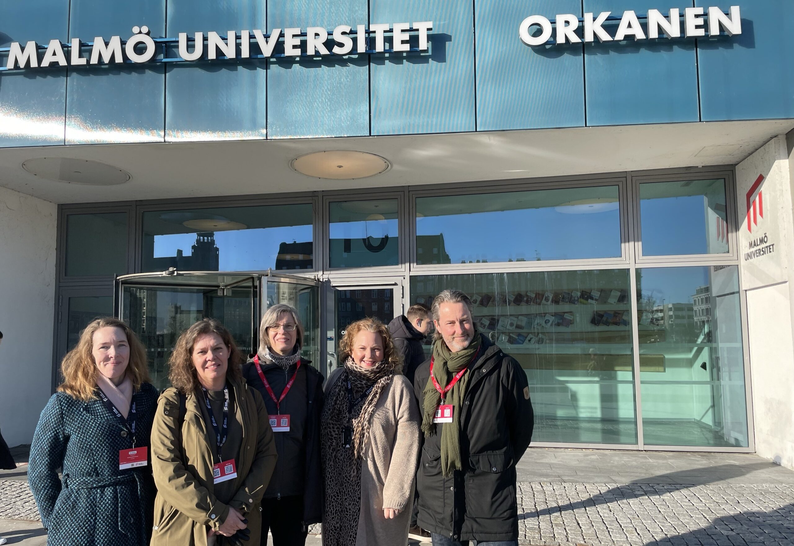 Fem personer står utanför entrén till Malmö universitet.