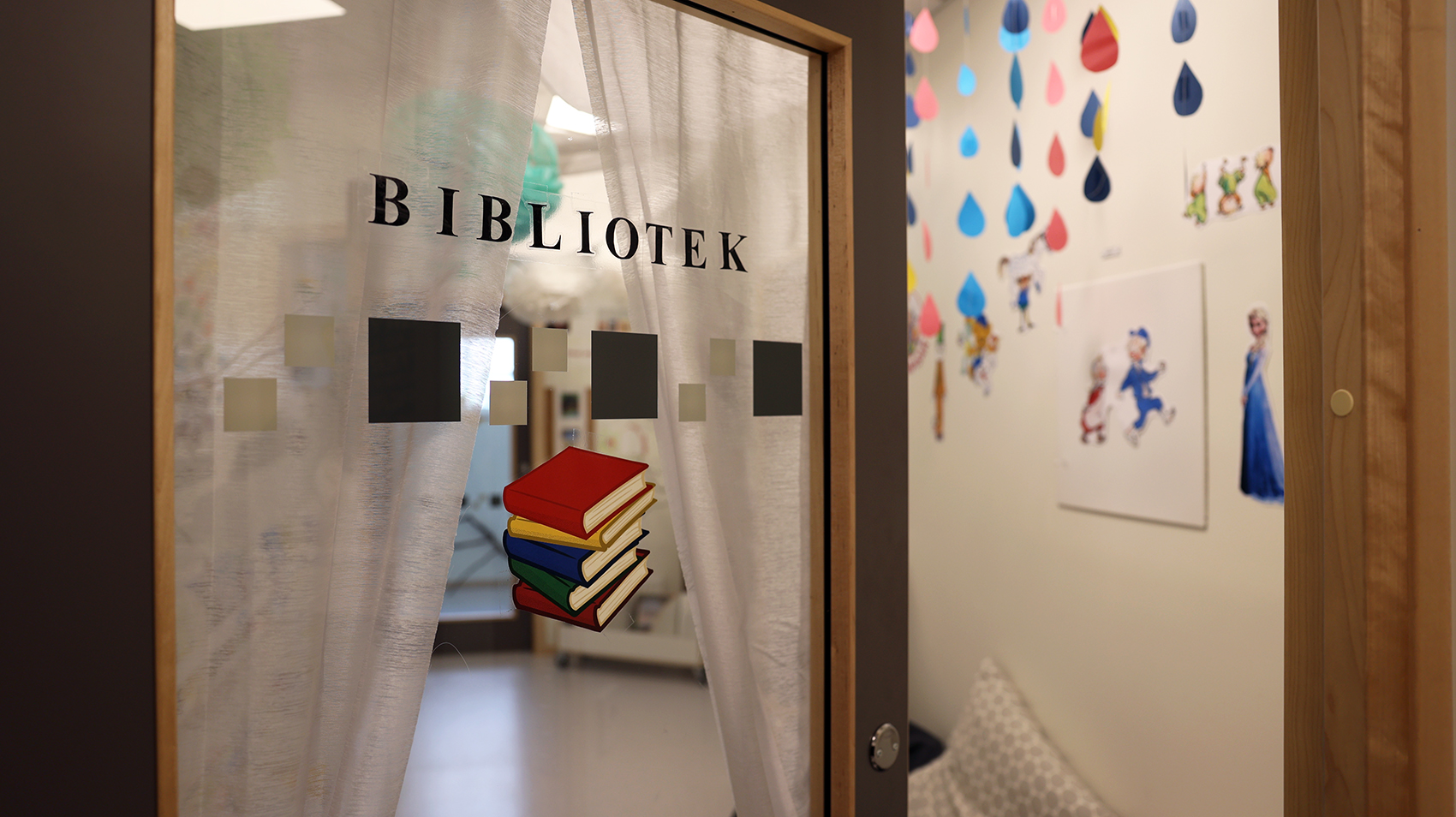 En dörr står på glänt in i biblioteket och genom en glipa i vita draperier kan man kika in.