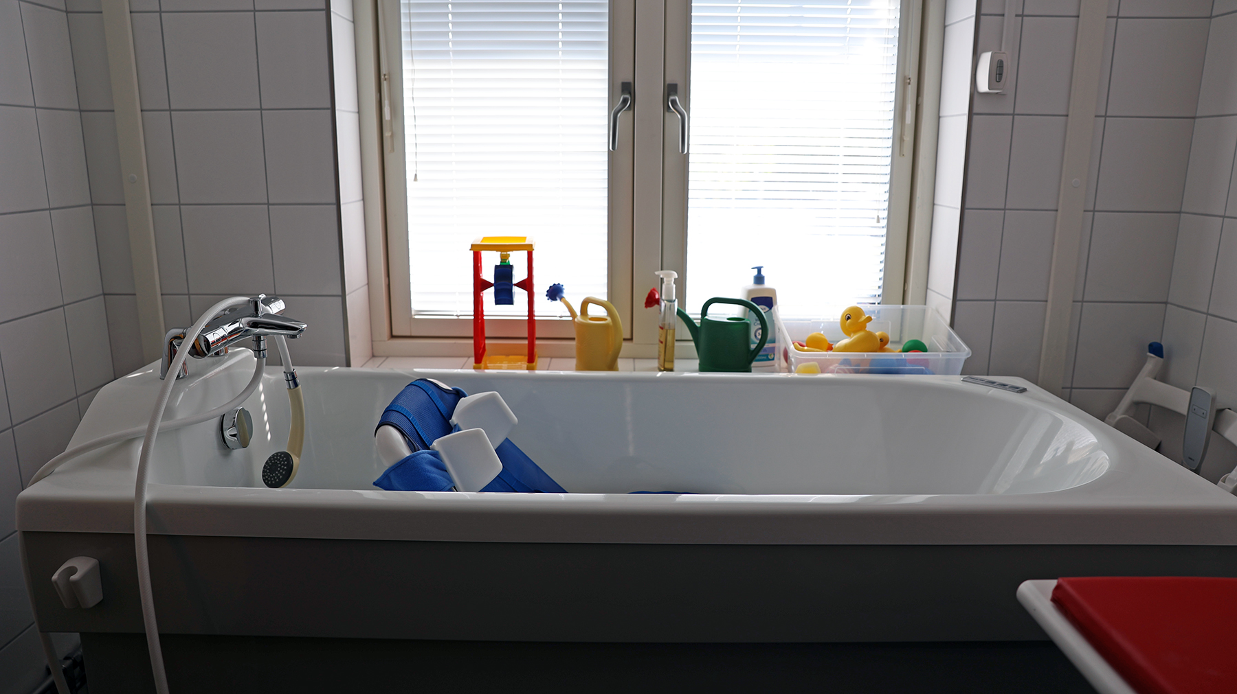 Ett badkar med sittstol i och olika badleksaker. I bakgrunden ett stort fönster.