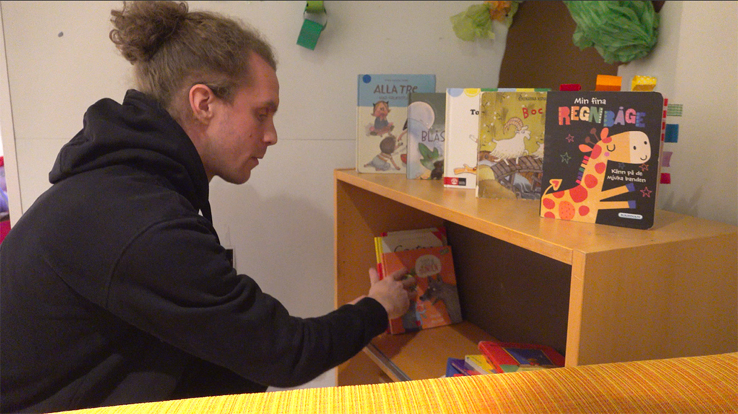 En förskolepedagog ställer böcker i en bokhylla.