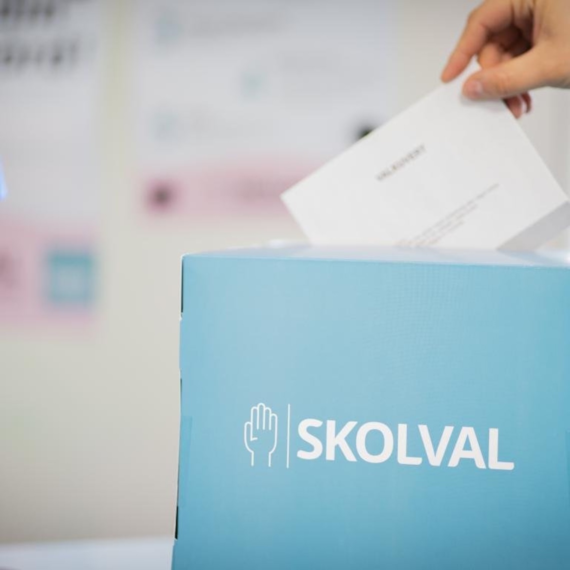 En hand lägger ett kuvert i en låda som det står 'skolval' på.