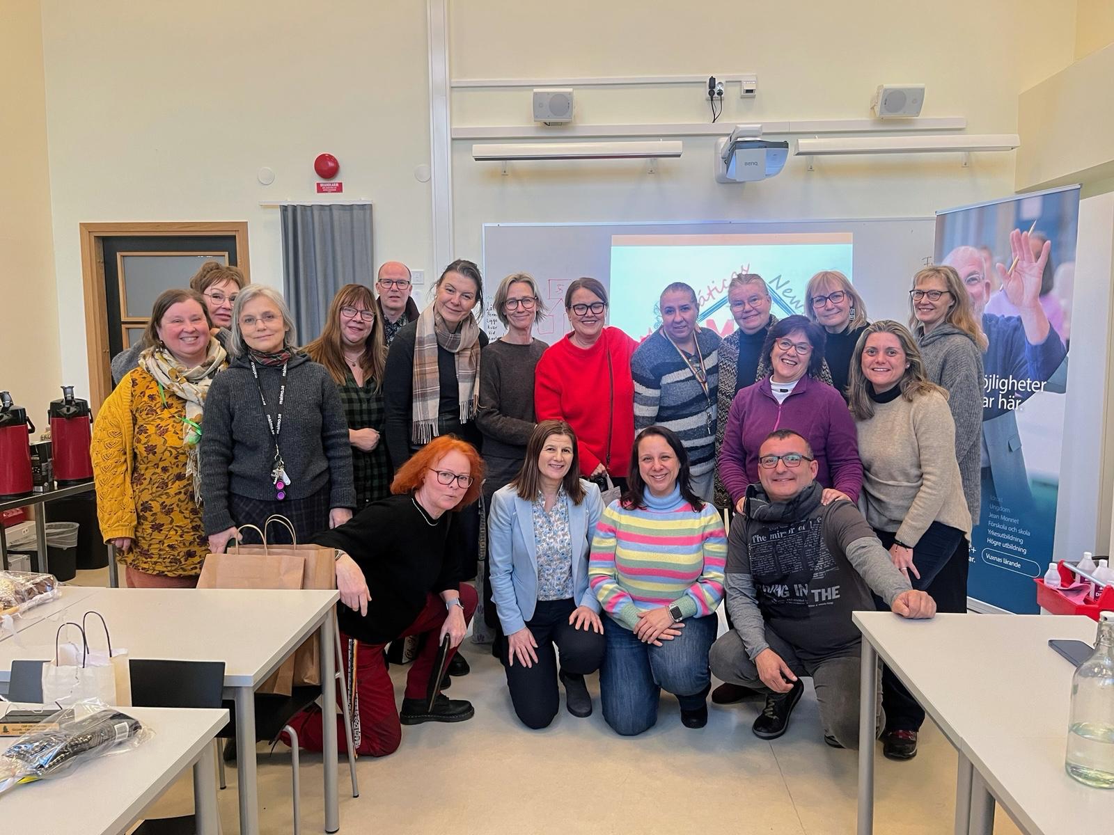 En grupp glada människor poserar för kameran i skolmiljö.