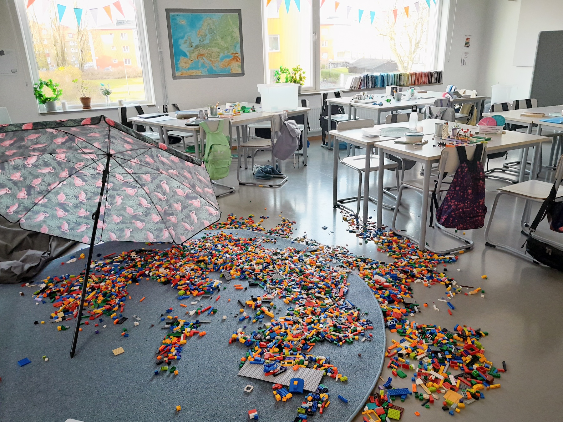 En stor mängd legobitar ligger utspridda över klassrumsgolvet.