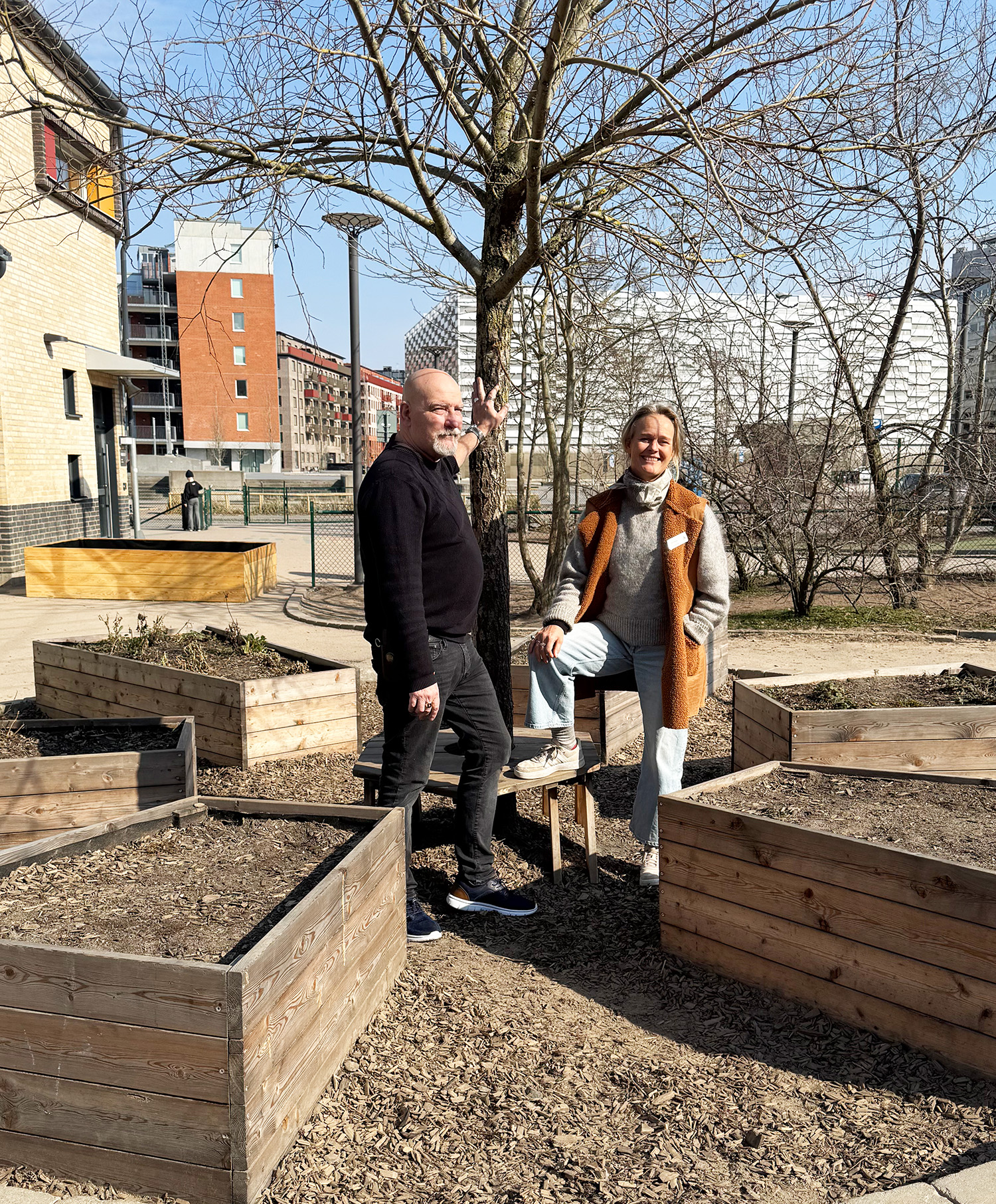 Två personer står utomhus i stadsmiljö, vid en samling odlingslådor.