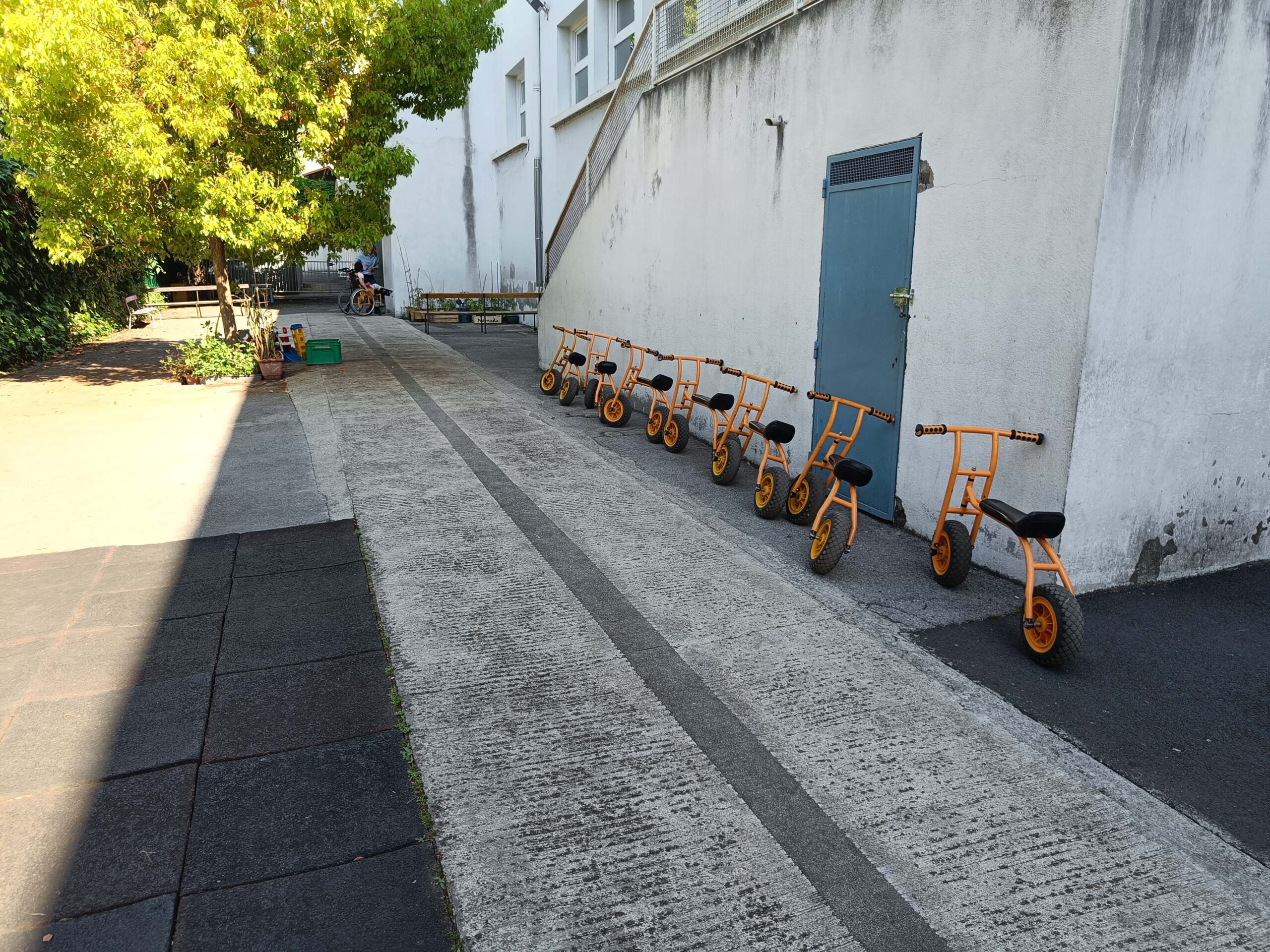 Flera gula barncyklar står prydligt uppradade mot en husvägg.