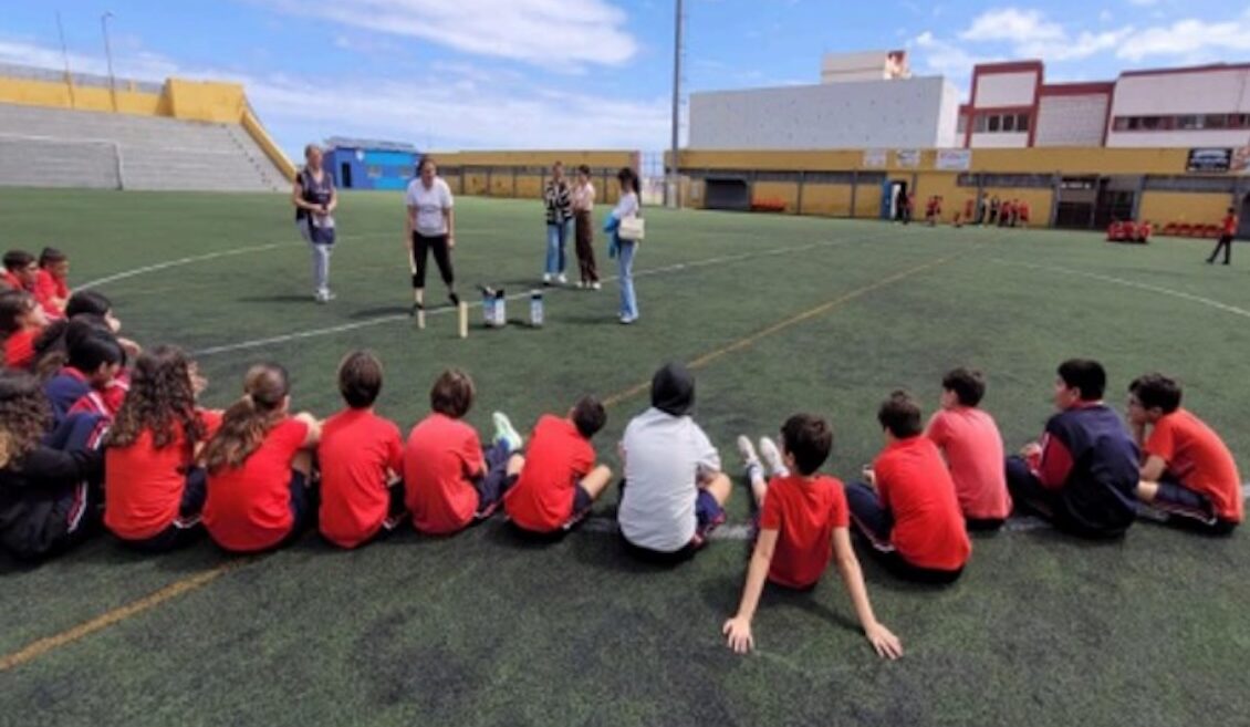 Elever sitter på en fotbollsplan och lyssnar på vuxna som ger instruktioner.