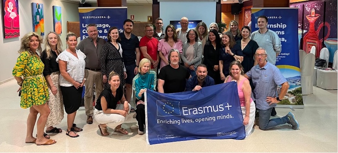 En grupp kursdeltagare poserar för kameran och håller upp en banderoll som det står 'Erasmus +' på.