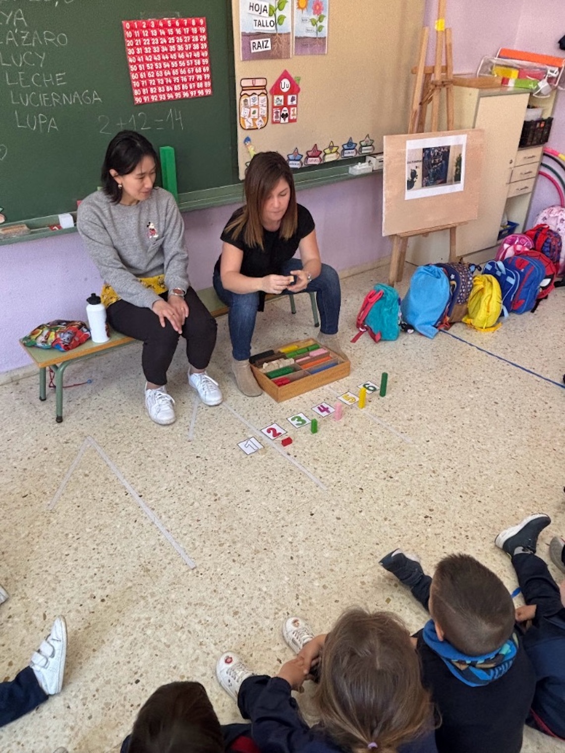 Elever sitter på golvet och lyssnar på lärare som undervisar i klassrum.