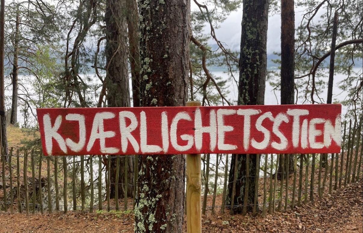 Kjærlighetsstien ('Kärleksstigen') står det handmålat på en träskylt i skogen.