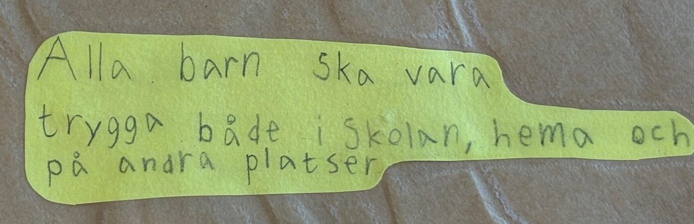 Texten 'Alla barn ska vara trygga både i skolan, hemma och på andra platser'.