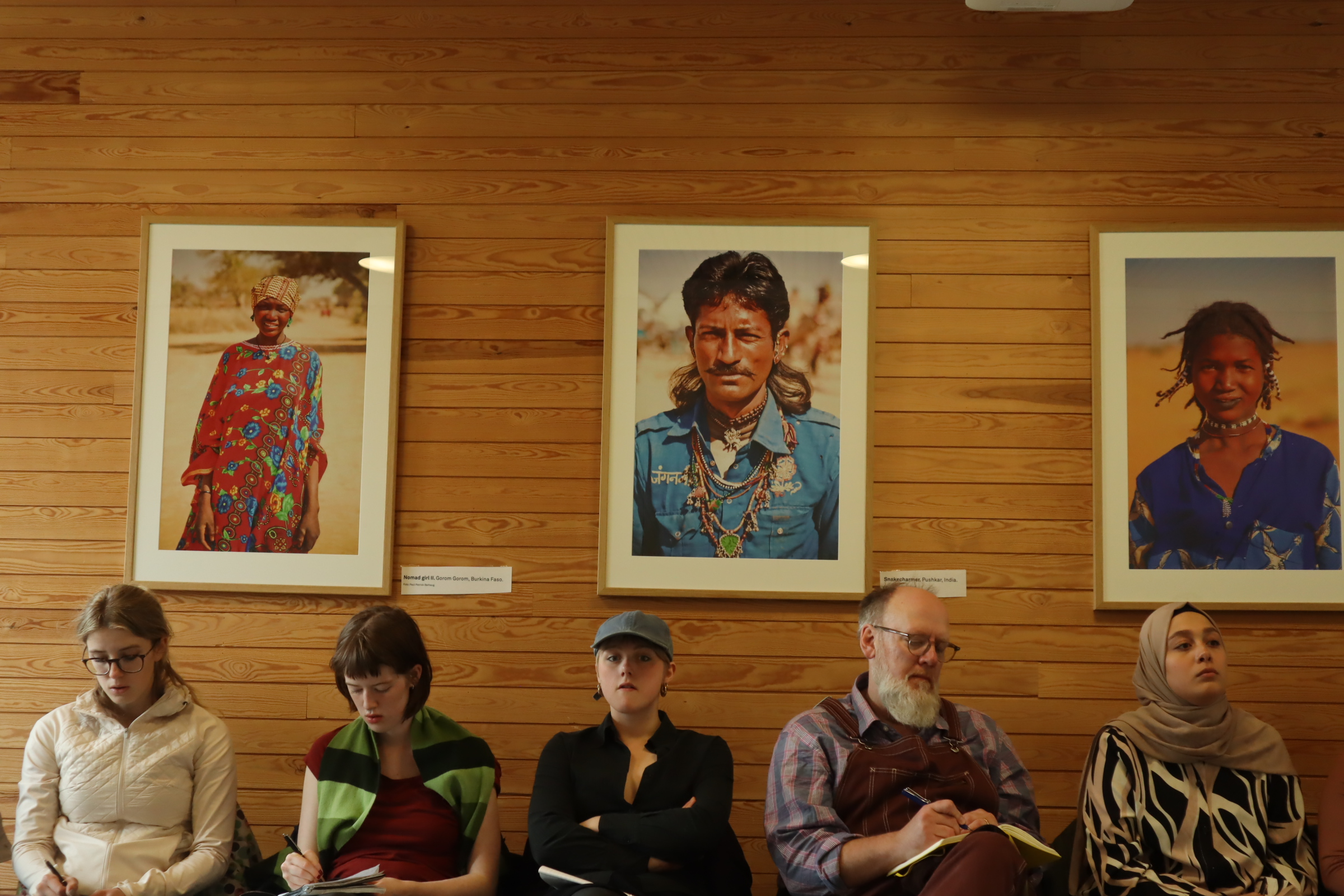 Elever och lärare sitter framför inramade personporträtt.