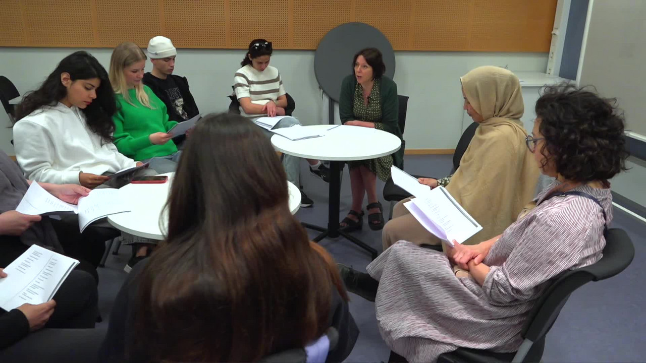 En grupp elever sitter tillsammans med en lärare runt ett par olika bord.