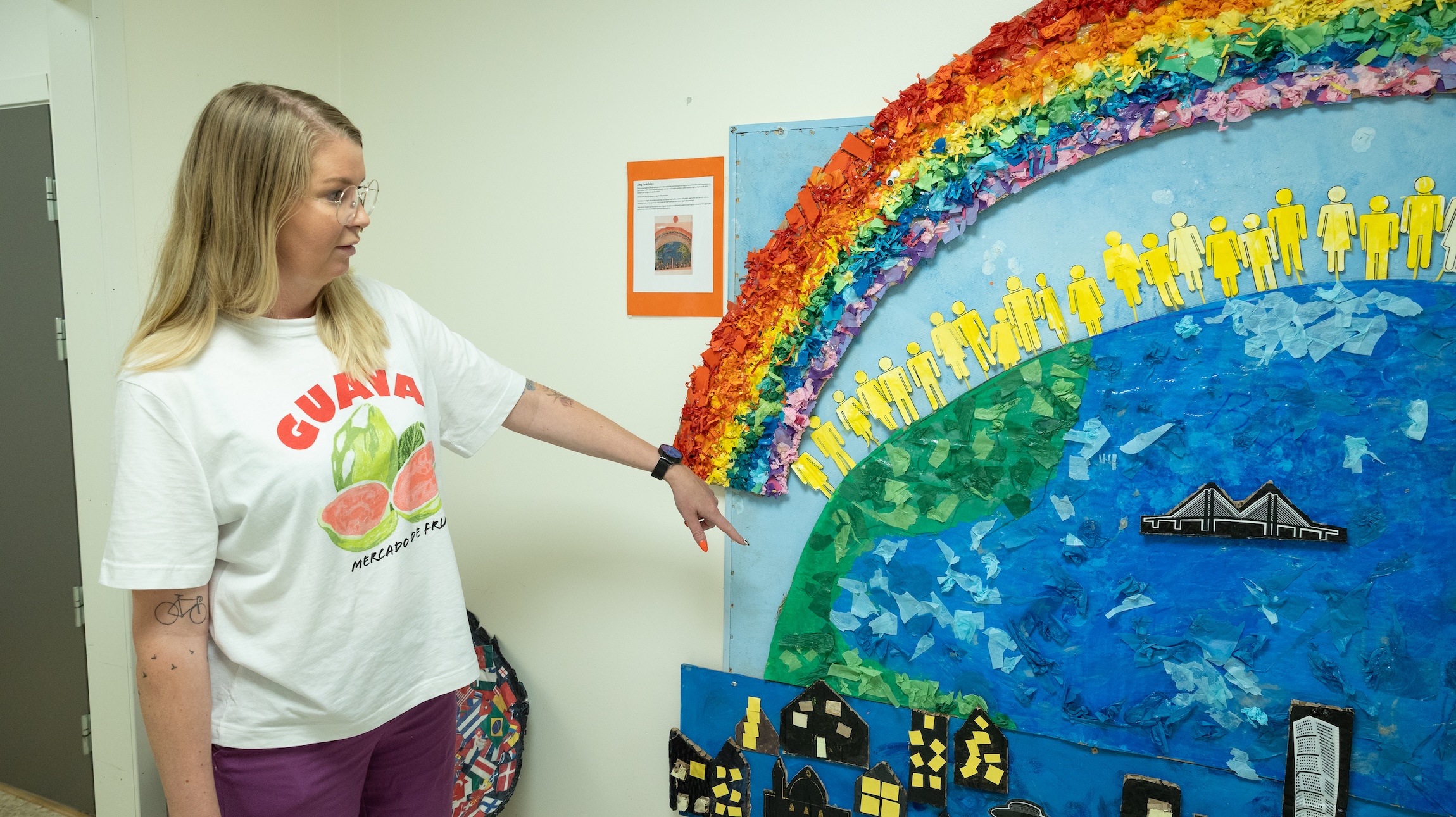 Iris Valgeirsdottir vid ett av elevernas konstverk; en avbildning av ett jordklot med en regnbåge över.