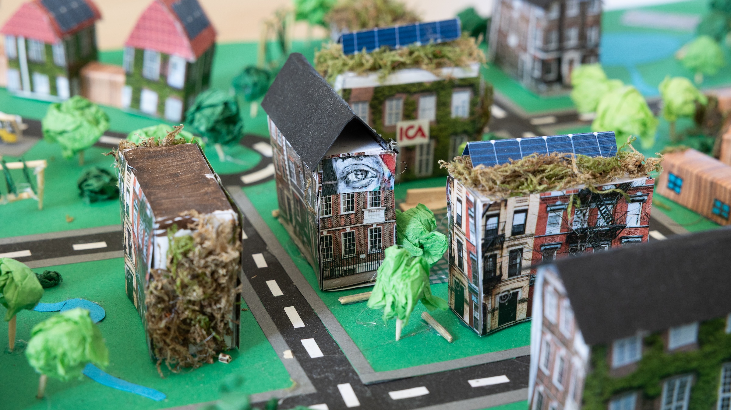 Elevernas modellbyggen av en hållbar stad; hus med växtlighet på väggar och solpaneler på taken.
