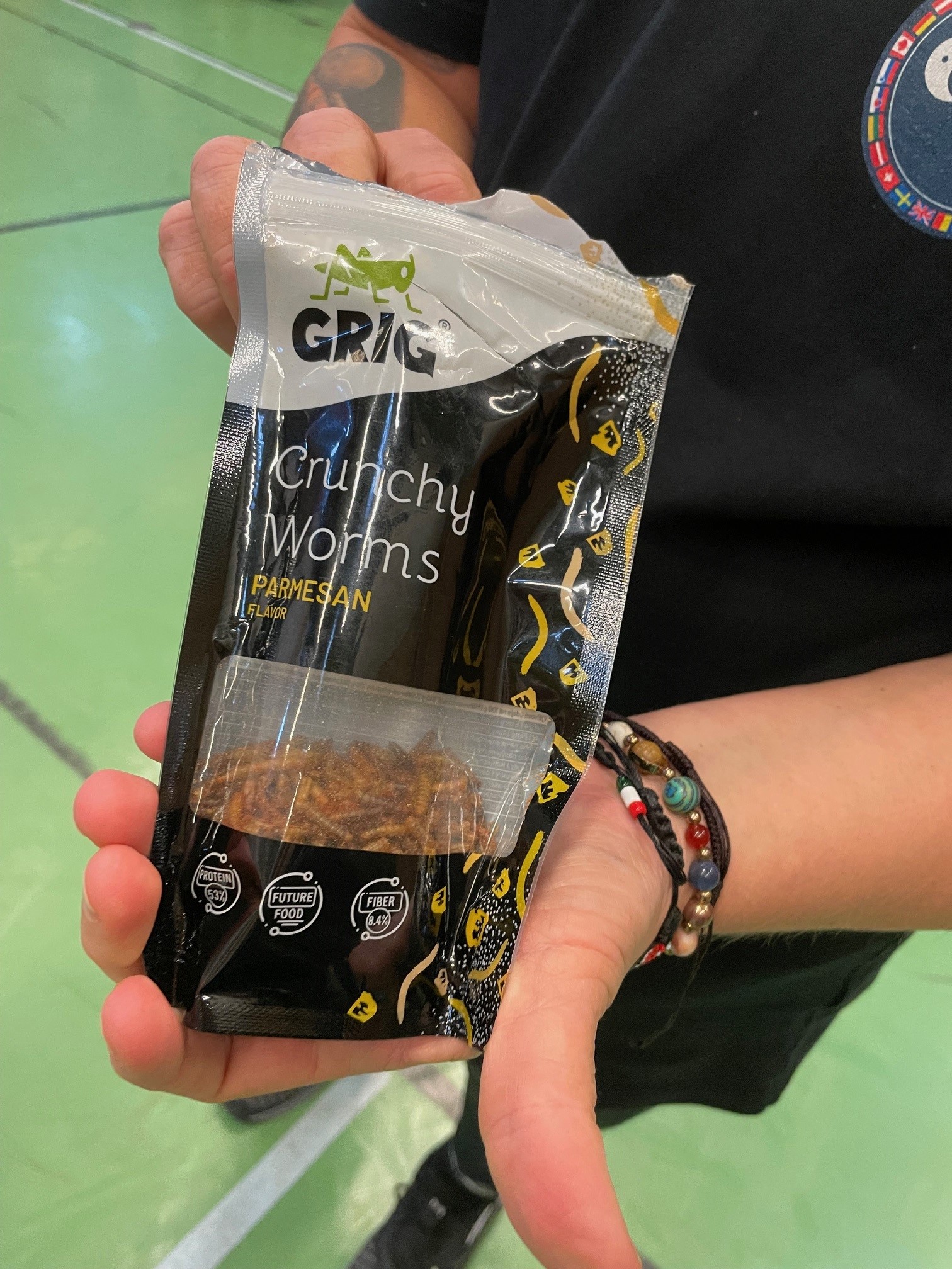 En hand håller en svart förpackning med texten ”GRIG Crunchy Worms Parmesan Flavor”, innehållande ätbara insekter.
