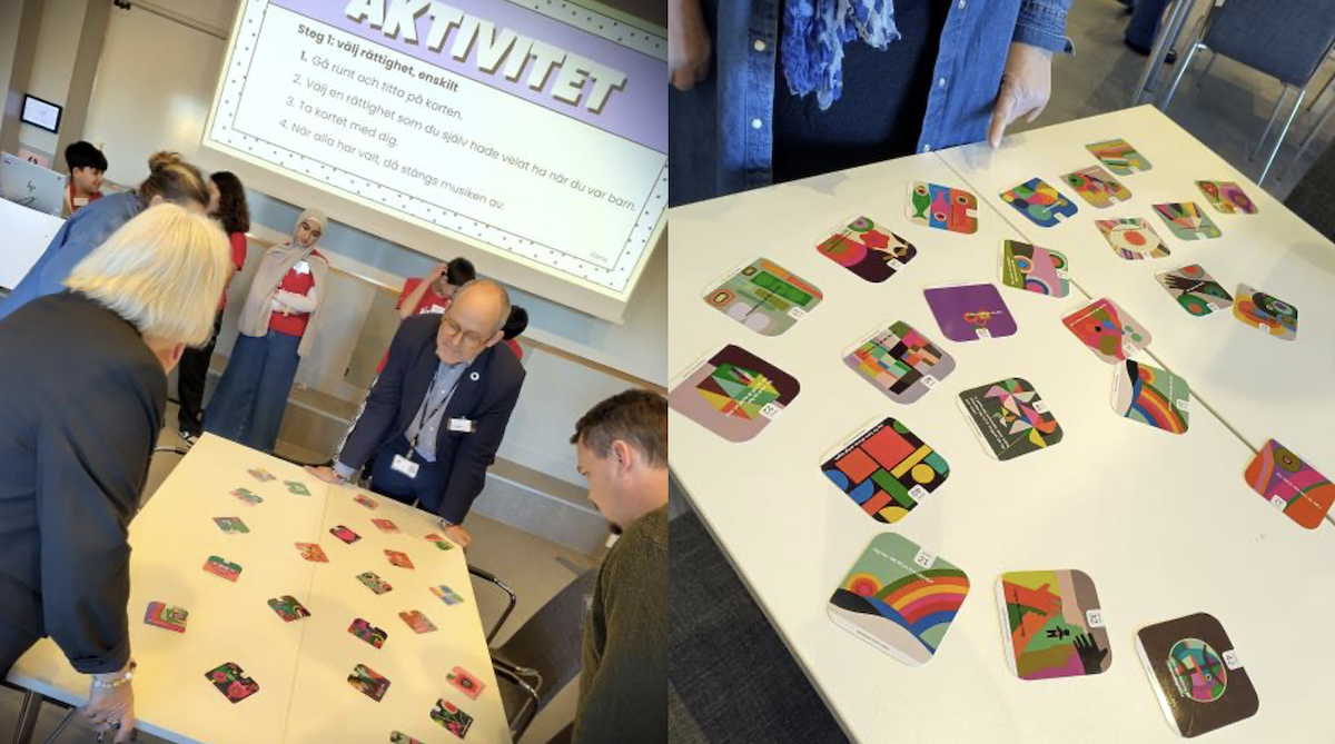 Deltagare står runt ett bord med färgglada kort som används i en workshopaktivitet under konferensen om demokrati och mänskliga rättigheter. På skärmen i bakgrunden syns ordet “Aktivitet”.