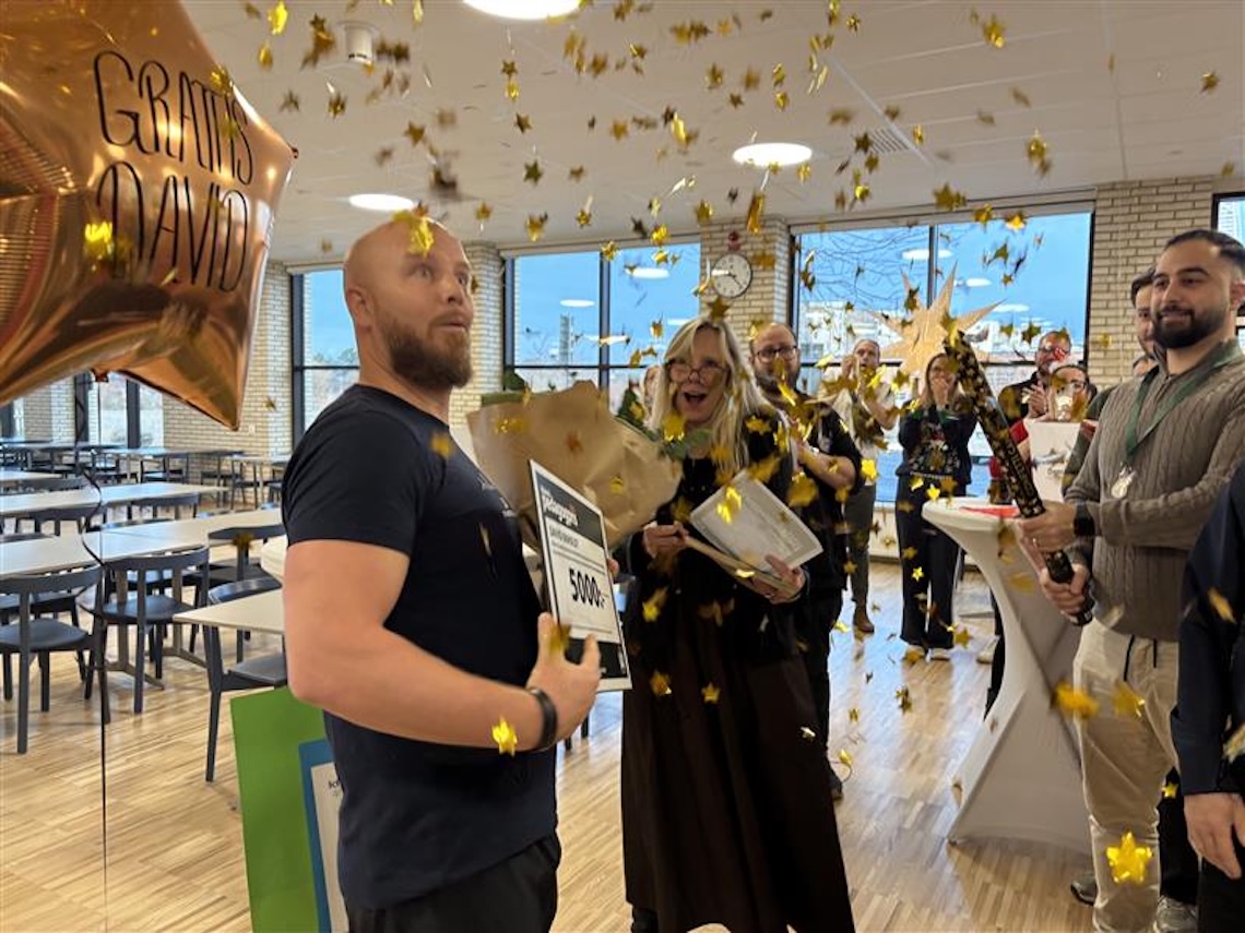 Firande i skolmatsal med konfetti, ballong med texten 'Grattis David' och prischeck på 5000 kronor.