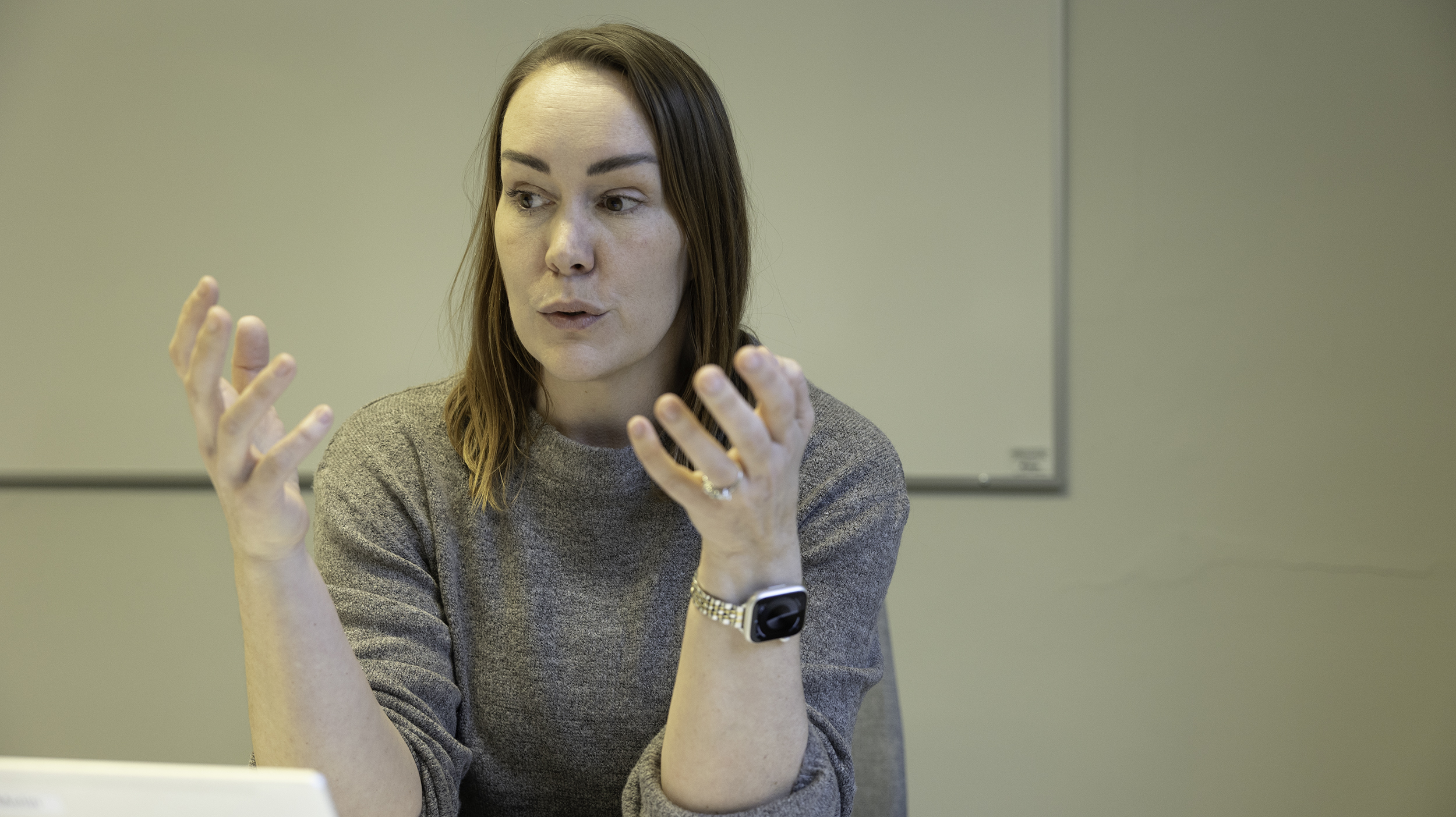 Person i grå tröja sitter framför whiteboard och gestikulerar med händerna.