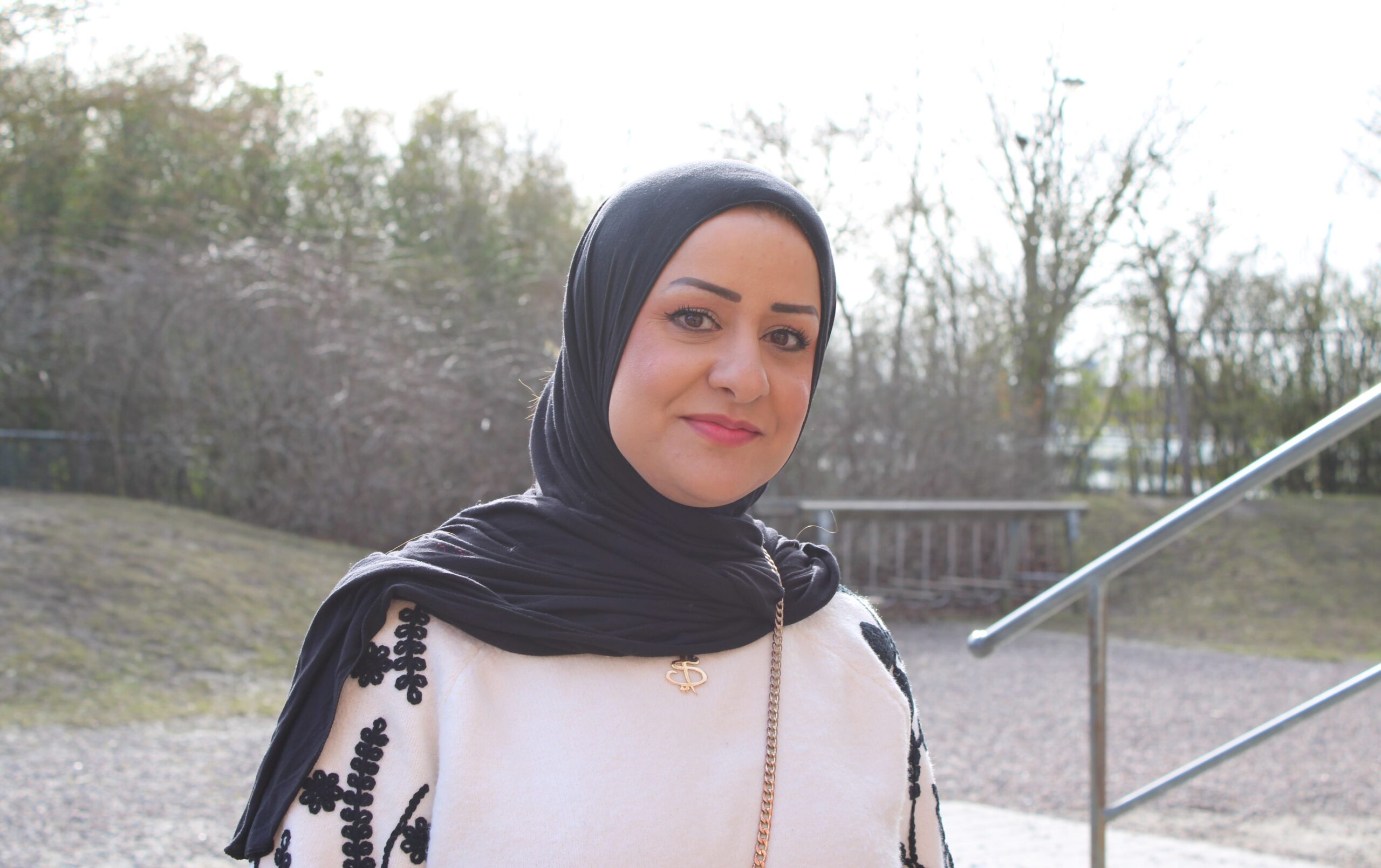 Person står utomhus med träd och grusgång i bakgrunden.