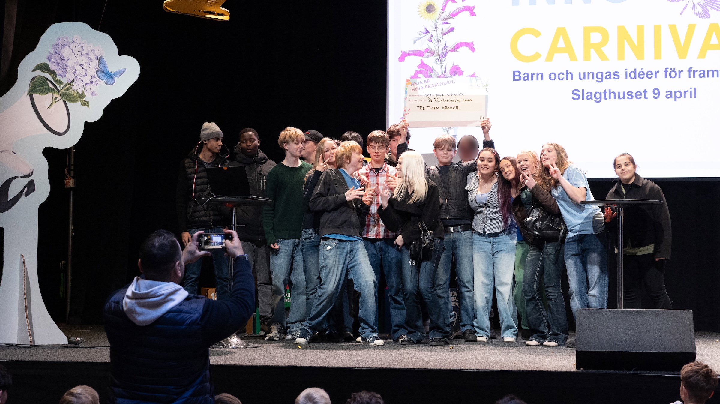 Grupp unga står på en scen och håller upp en skylt framför en stor skärm med text om Carnival och barn och ungas idéer.