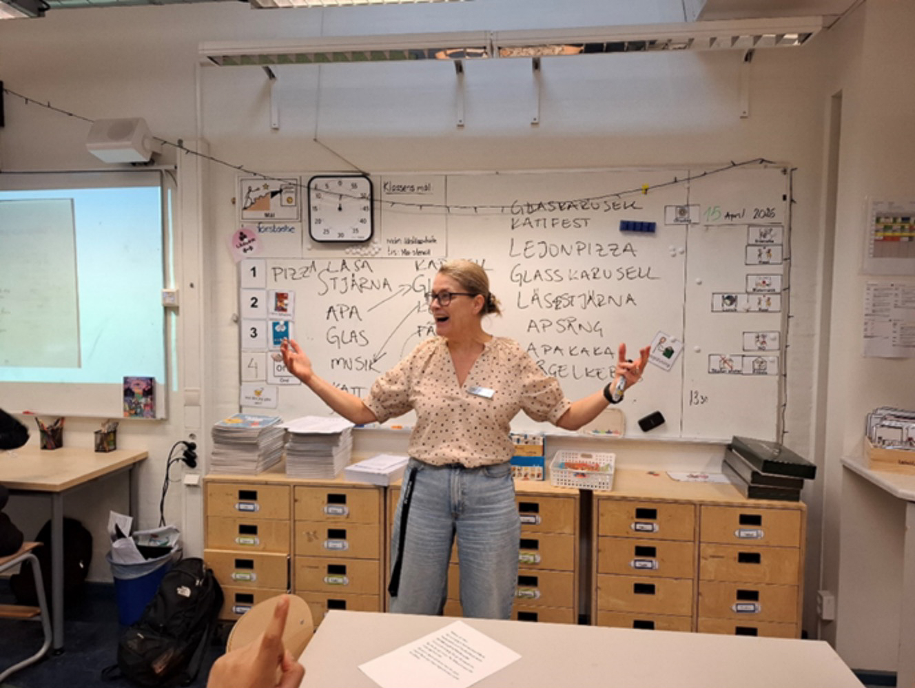 Person står i ett klassrum och gestikulerar framför en whiteboard med text och schemainnehåll.