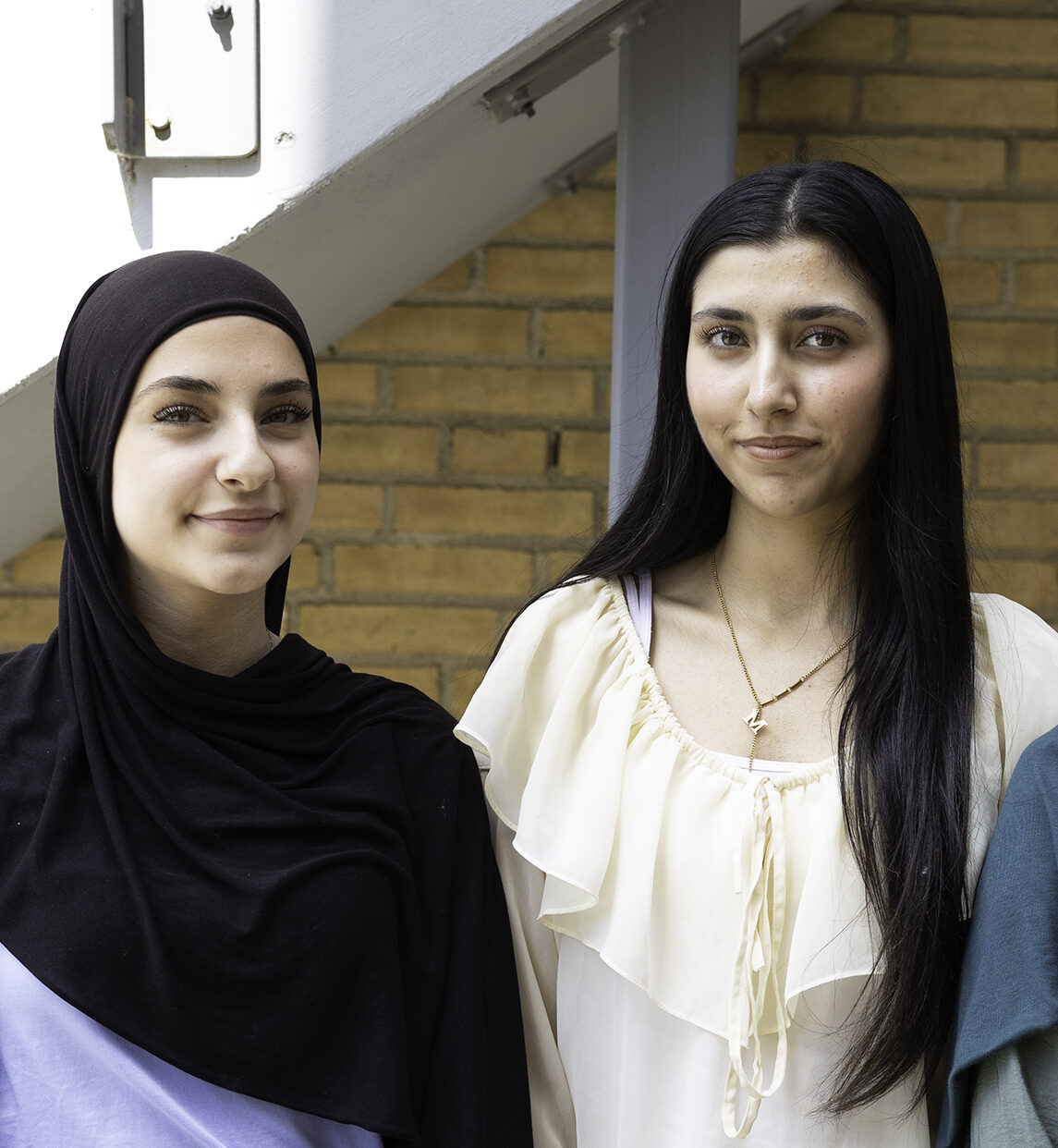 Två personer står framför en tegelvägg och en trappa utomhus.