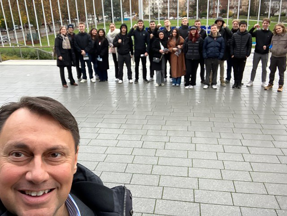 En lärare står längst fram och tar en bild. I bakgrunden står hans elever.