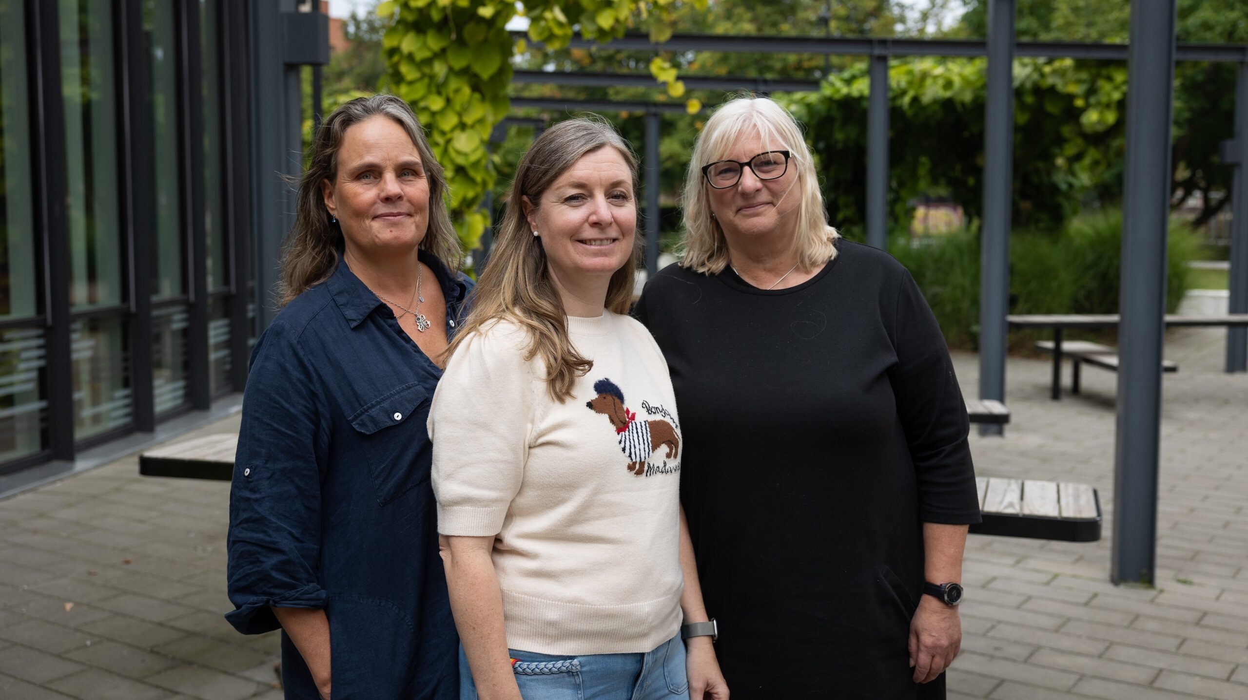 Tre pedagoger i skolmiljö utomhus framför grönska och skolbyggnad.