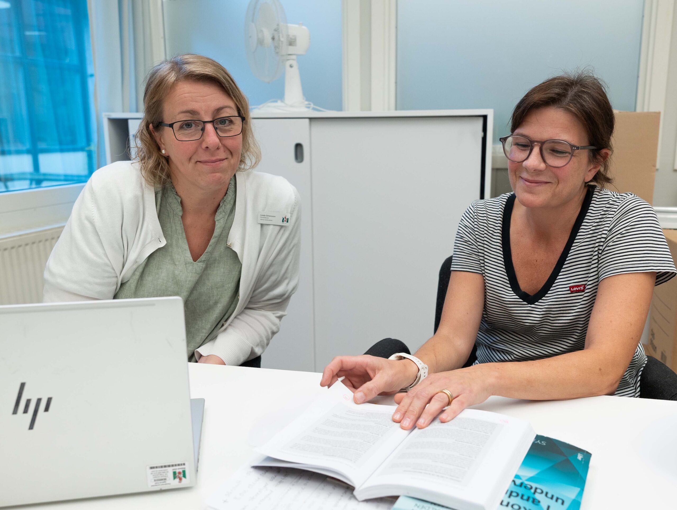 Två medarbetare diskuterar innehållet i en bok vid en dator.