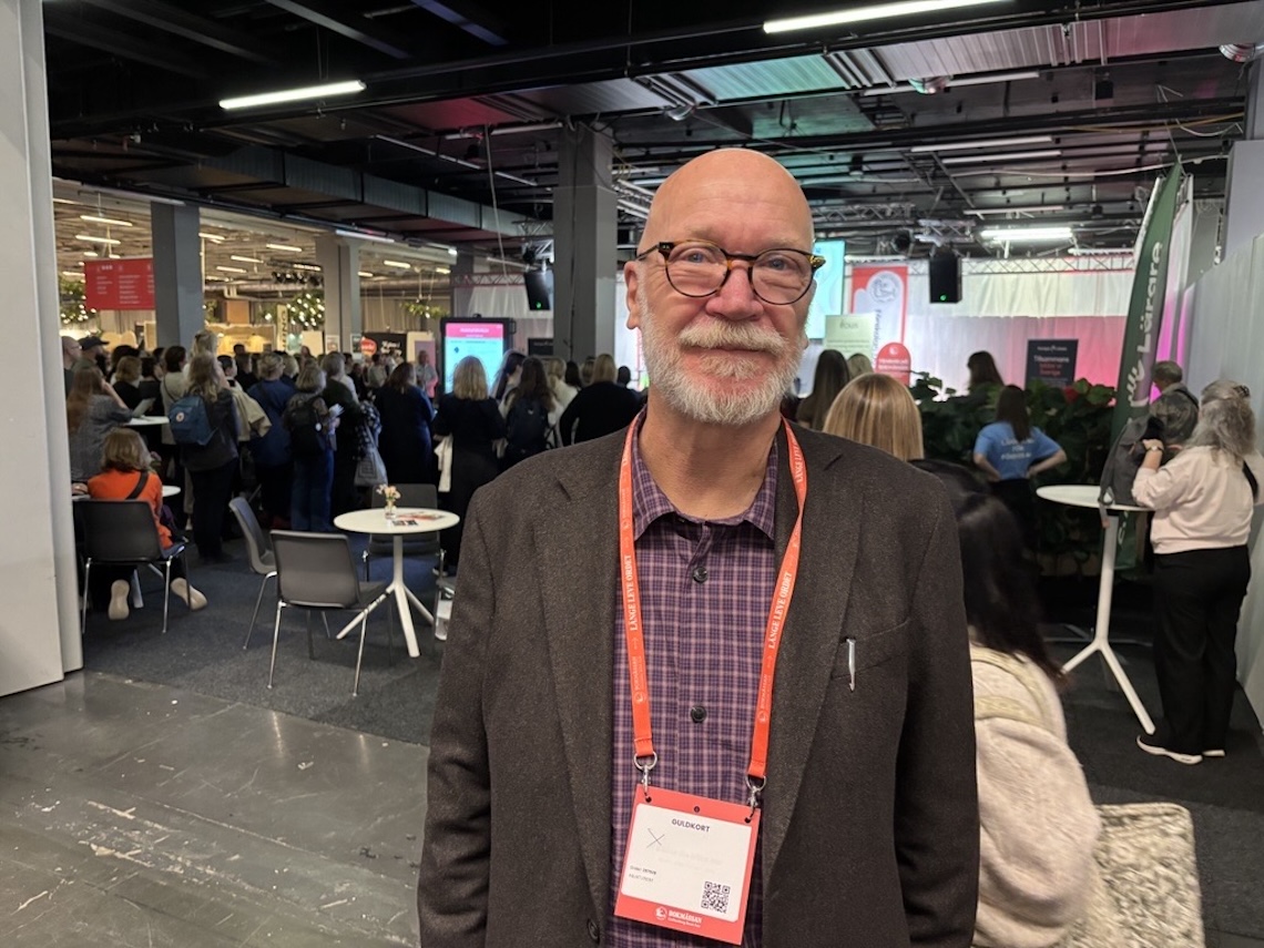 Ulf Malmqvist med konferensbadge fotograferad på bokmässan i Göteborg med föreläsningsscen i bakgrunden.